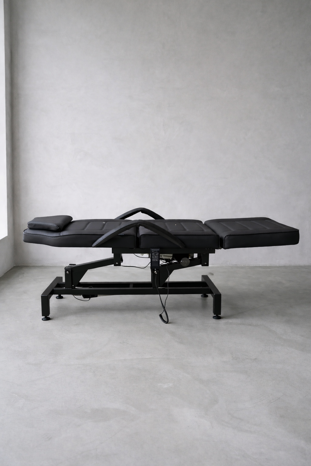 Multi-purpose clinic bed in black vinyl with segmented cushioning for injectables, IPL and advanced skin treatments