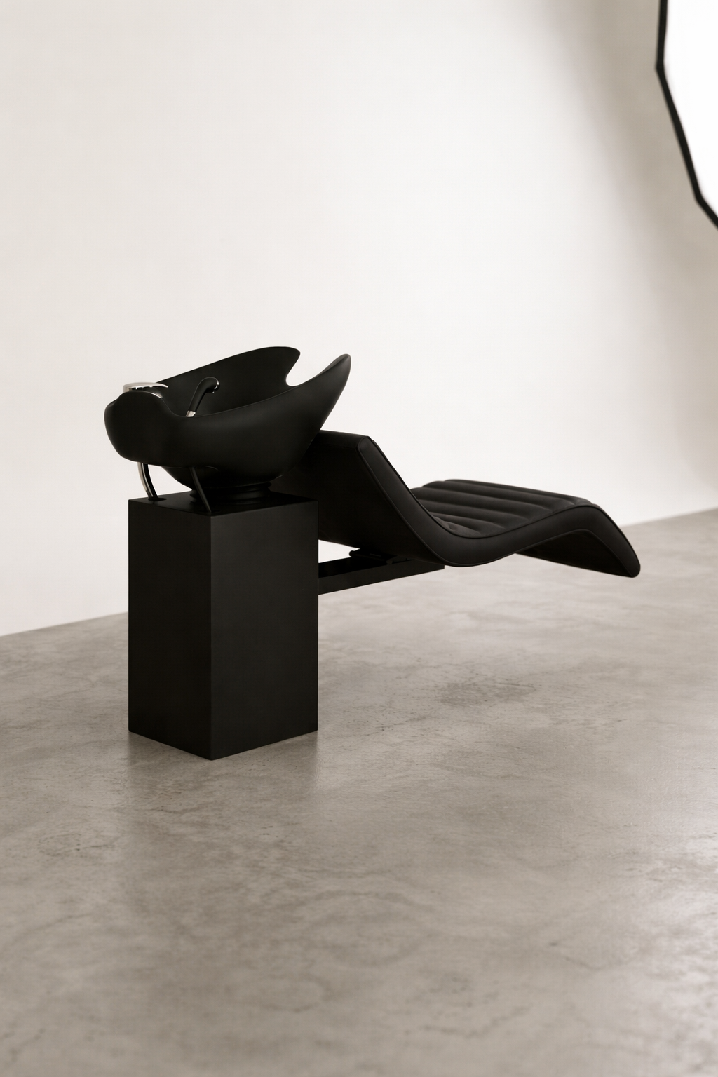 Modern shampoo basin unit with black vinyl upholstery and curved reclining seat, minimalist salon furniture design